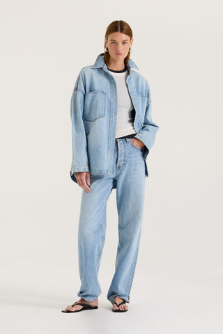 Model wearing a light blue denim jacket with a white long sleeve underneath and light blue denim jeans on a white background
