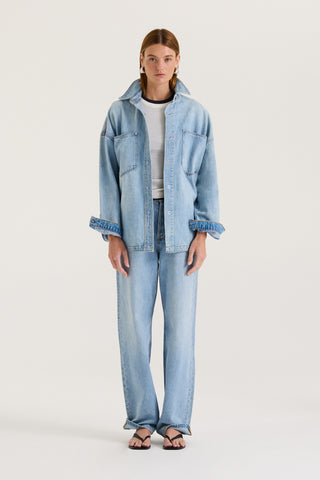 Model wearing a light blue denim jacket with a white long sleeve underneath and light blue denim jeans on a white background