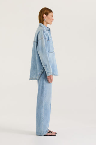 Side view of a model wearing a light blue denim jacket and light blue denim jeans on a white background