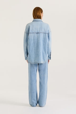Back view of a model wearing a light blue denim jacket and light blue denim jeans on a white background