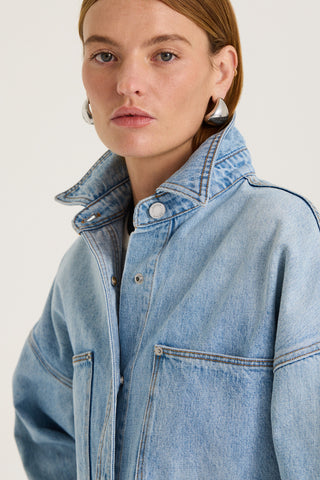 Close up view of a model wearing a light blue denim jacket on a white background