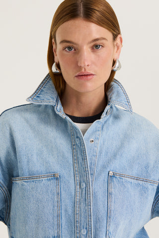 Close up view of a model wearing a light blue denim jacket on a white background