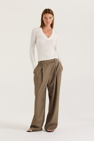 Model wearing a white long-sleeve top and taupe wide-leg pants on a white background