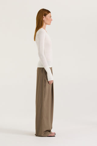 Side view of a model wearing a white long-sleeve top and taupe wide-leg pants on a white background
