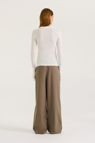 Back view of a model wearing a white long-sleeve top and taupe wide-leg pants on a white background