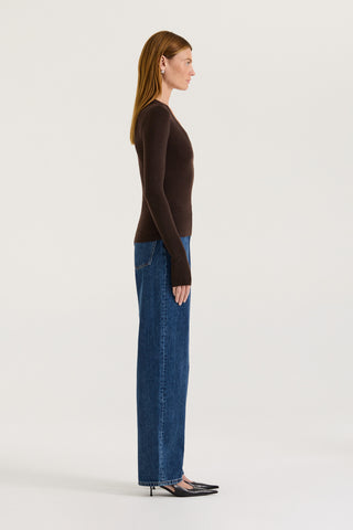 Side view of a model wearing a chocolate long-sleeve top and blue jeans on a white background