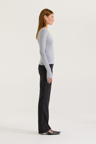 Side view of a model wearing a grey long sleeve top and black jeans on a white background