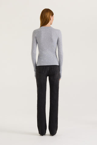 Back view of a model wearing a grey long sleeve top and black jeans on a white background