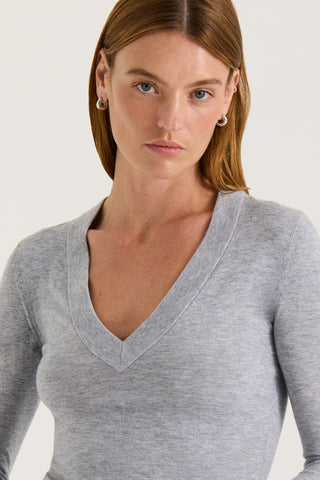 Model wearing a grey long sleeve V-neck top on a white background