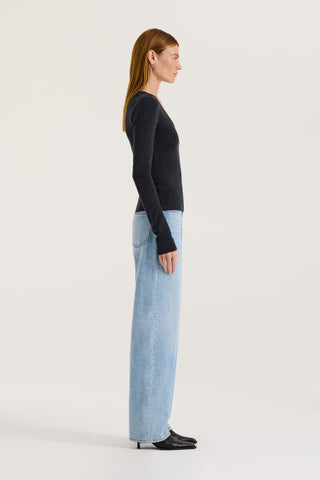 Side view of a model wearing a charcoal long-sleeve scoop top and light blue jeans on a white background