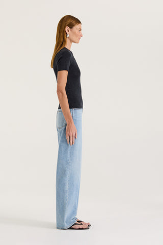 Side view of a model wearing a charcoal t-shirt and light blue jeans on a white background