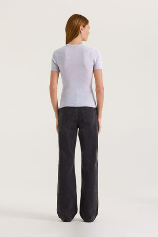 Back view of a model wearing a light grey fitted t-shirt and black jeans on a white background
