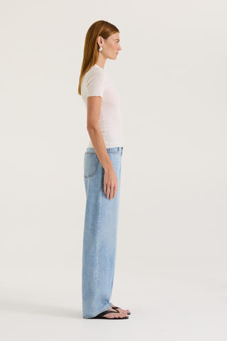 Side view of a model wearing a white fitted t-shirt and light blue jeans on a white background