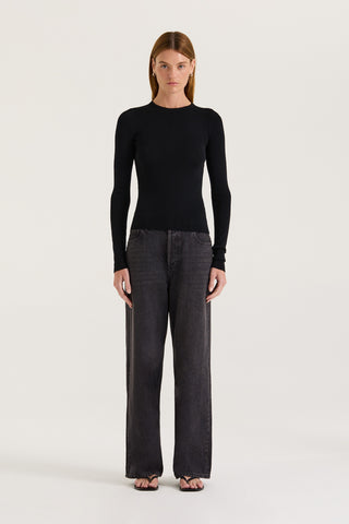 A model wearing a black long-sleeve top and black wide-leg jeans on a white background 