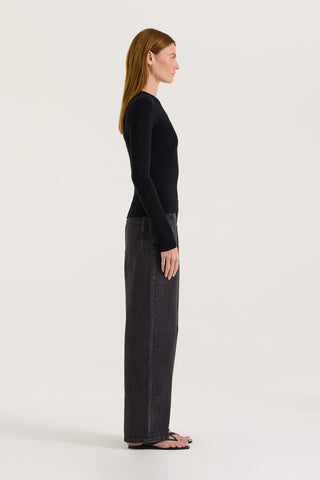 Side view of a model wearing a black long-sleeve top and black wide-leg jeans on a white background 