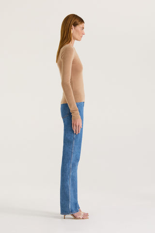 Side view of a model wearing a tanned long sleeve top and blue jeans with a white background