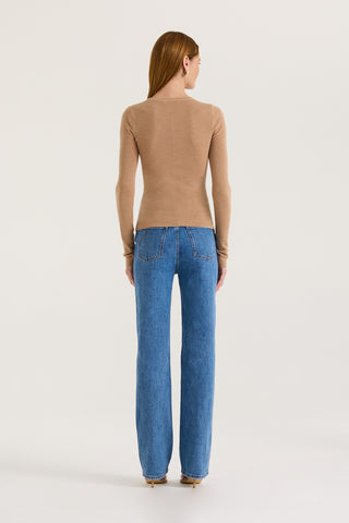 Back view of a model wearing a tanned long sleeve top and blue jeans with a white background