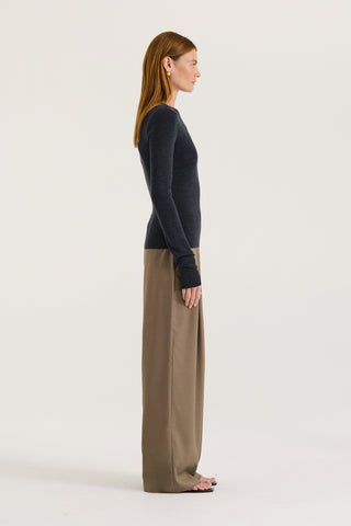 Side view of a model wearing a charcoal long sleeve top and taupe pants on a white background