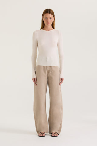 A model wearing a white long sleeve top and tan wash jeans on a white background