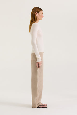 Side view of a model wearing a white long sleeve top and tan wash jeans on a white background