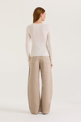 Back view of a model wearing a white long sleeve top and tan wash jeans on a white background