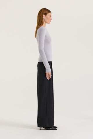 Side view of a model wearing a light grey long sleeve top and black pants on a white background