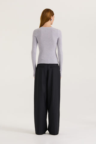 Back view of a model wearing a light grey long sleeve top and black pants on a white background