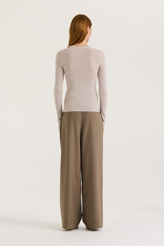 Back view of a model wearing a light grey long sleeve top and taupe pants against a white background