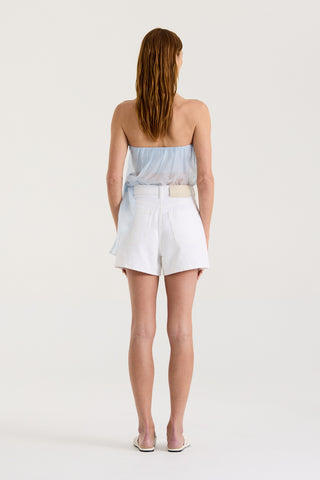 Back view of a model wearing a strapless light blue sheer top and white denim shorts on a white background