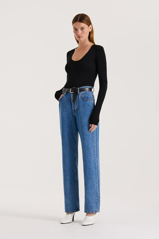 Model wearing a black scoop neck long sleeve top and indigo straight leg jeans with a belt on a white background