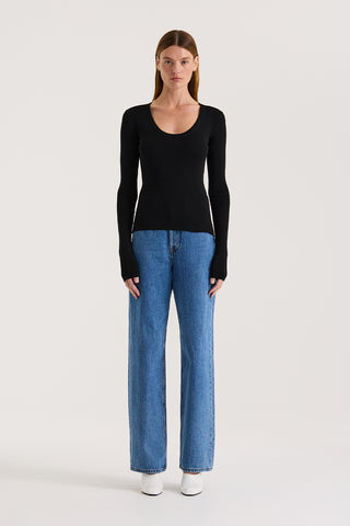 Model wearing a black scoop neck long sleeve top and indigo straight leg jeans on a white background