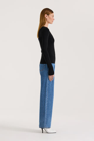 Side view of a model wearing a black long sleeve top and indigo straight leg jeans on a white background