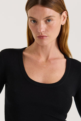 Close up view of a model wearing a black scoop neck long sleeve top on a white background