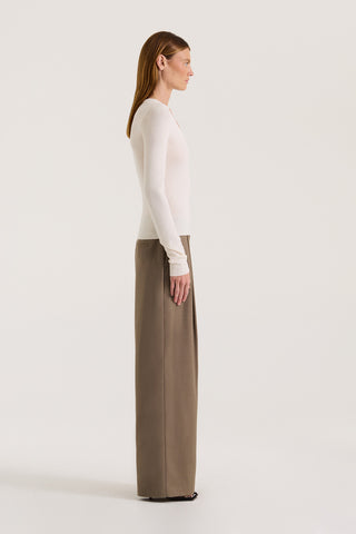 Side view of a model wearing a cream long-sleeve scoop neck top and taupe wide-leg pants on a white background