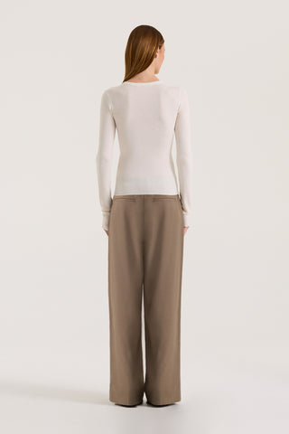 Back view of a model wearing a cream long-sleeve top and taupe wide-leg pants on a white background