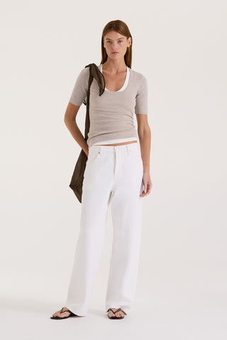 Model wearing a light grey fitted t-shirt with a white tank underneath and white wide-leg jeans on a white background