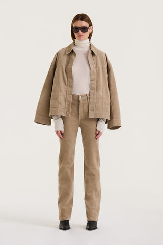 Model wearing a beige corduroy jacket, white turtleneck, and beige pants on a white background