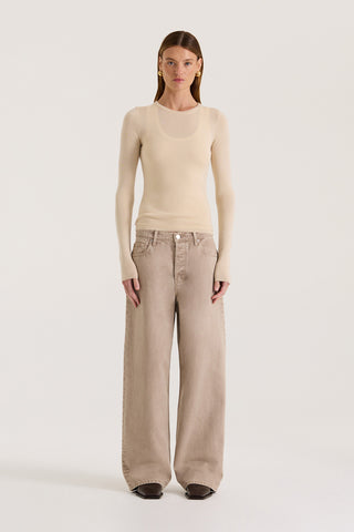 Model wearing a beige fitted long sleeve top with a white tank underneath and light brown pants on a white background