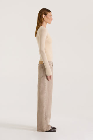 Side view of a model wearing a beige fitted long sleeve top and light brown pants on a white background