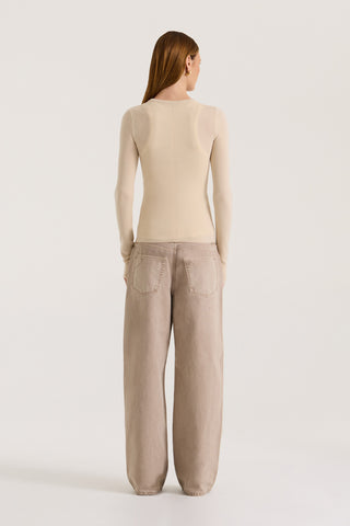 Back view of model wearing a beige fitted long sleeve top and light brown pants on a white background