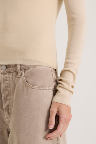 Close up few of a model wearing a beige long-sleeve top and light brown jeans on a white background