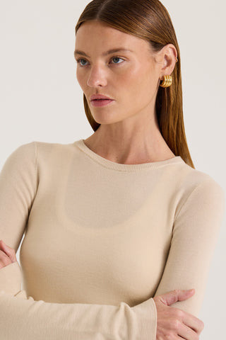 Close up view of a model wearing a beige long sleeve top on a white background