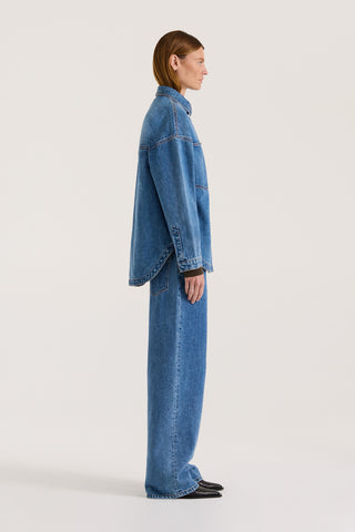 Side view of a model wearing a indigo wash denim jacket with the matching denim jeans on a white background