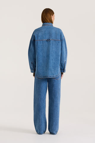 Back view of a model wearing a indigo wash denim jacket with the matching denim jeans on a white background