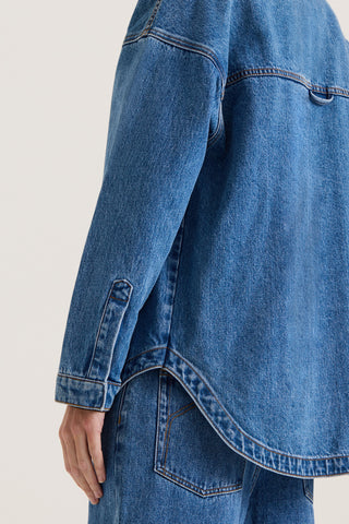 Close up back view of a model wearing an indigo wash denim jacket on a white background