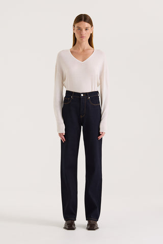 Model is wearing a white long-sleeve top and dark indigo straight leg, high rise jeans on a white background