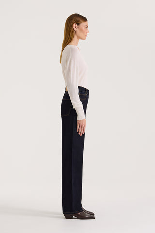 Side view of a model wearing a white long-sleeve top and dark indigo straight leg, high rise jeans on a white background