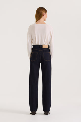 Back view of a model wearing a white long-sleeve top and dark indigo straight leg, high rise jeans on a white background