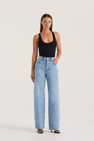Petite model wearing light wash straight-leg, high-rise petite jeans and a black tank top against a white background.