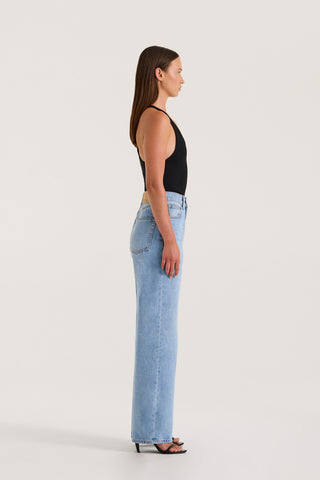 Side view of petite model wearing light wash straight-leg, high-rise petite jeans and a black tank top against a white background.